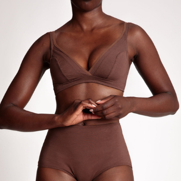 A midriff closeup of a dark-skinned Black feminine person wearing skin-colored organic cotton wireless bra and matching panty and garter from Nubian Skin